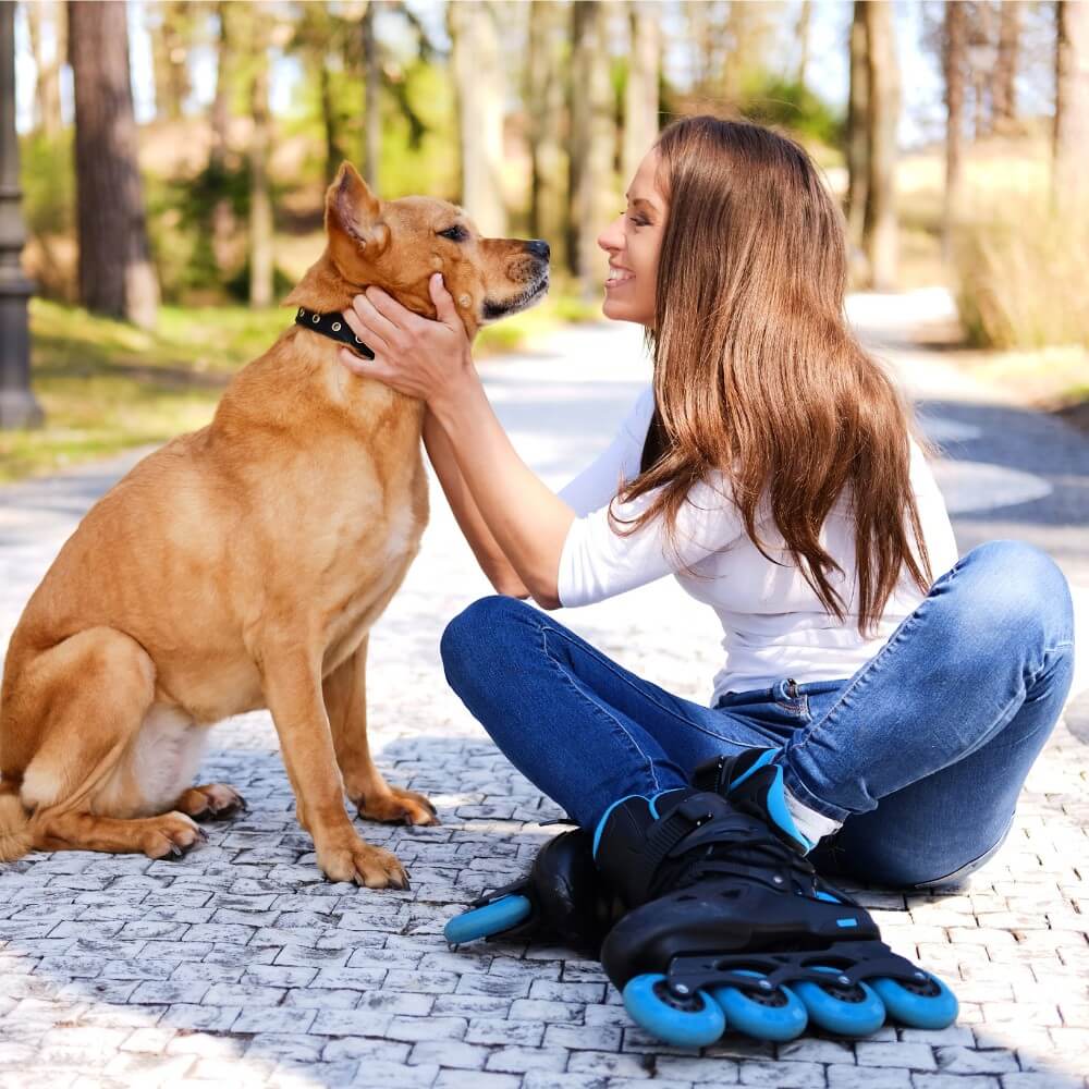 Mujer sonriente acariciando a su perro color miel, reflejando el vínculo entre humanos y mascotas en un parque soleado.