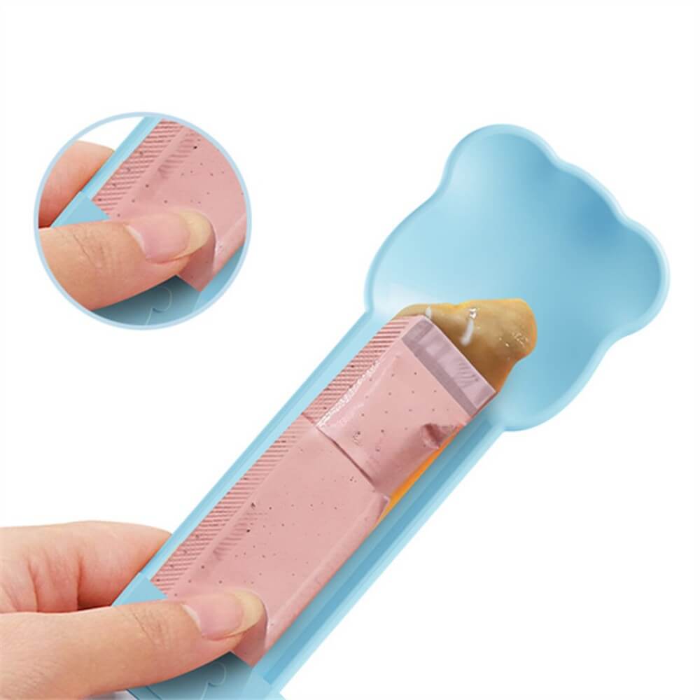 Mano que muestra el funcionamiento de la cuchara exprimidora azul, indica cómo deslizar el sachet de snack cremoso para exprimirlo