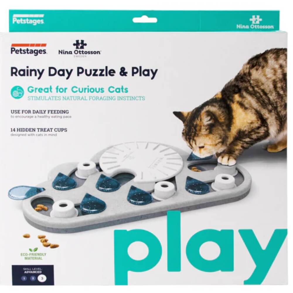 Empaque frontal del puzzle interactivo para gatos Nina Ottosson Rainy Day Nivel 3. Tablero gris con gato atigrado y marca Petstages