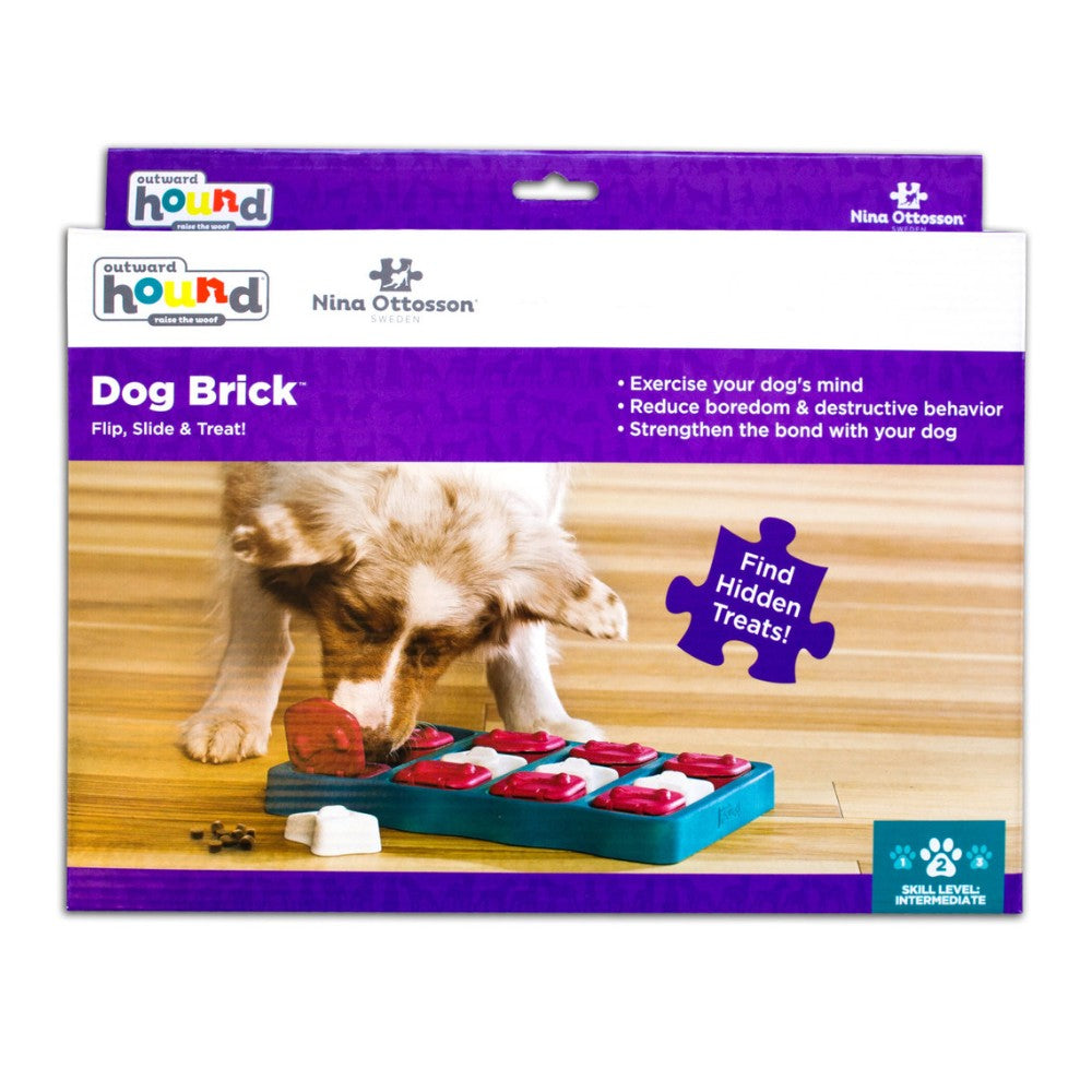 Caja Outward Hound Nina Ottosson Dog Brick con foto de perro usando un puzzle de base azul petróleo con piezas rojas y blancas